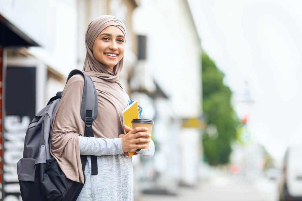 Muslim girl student drinking coffee on street before studying