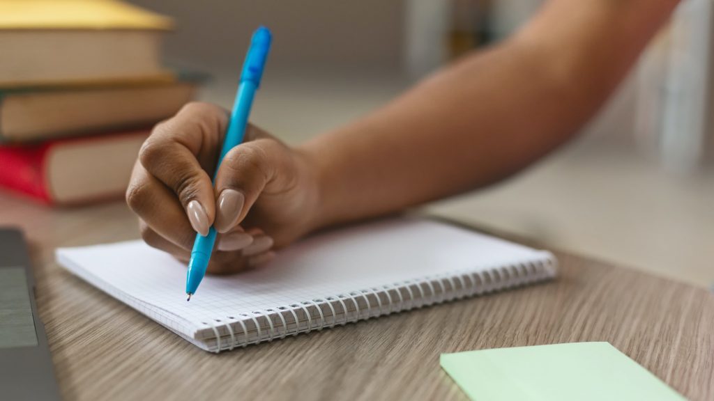 Teen black girl writing notes in notebook